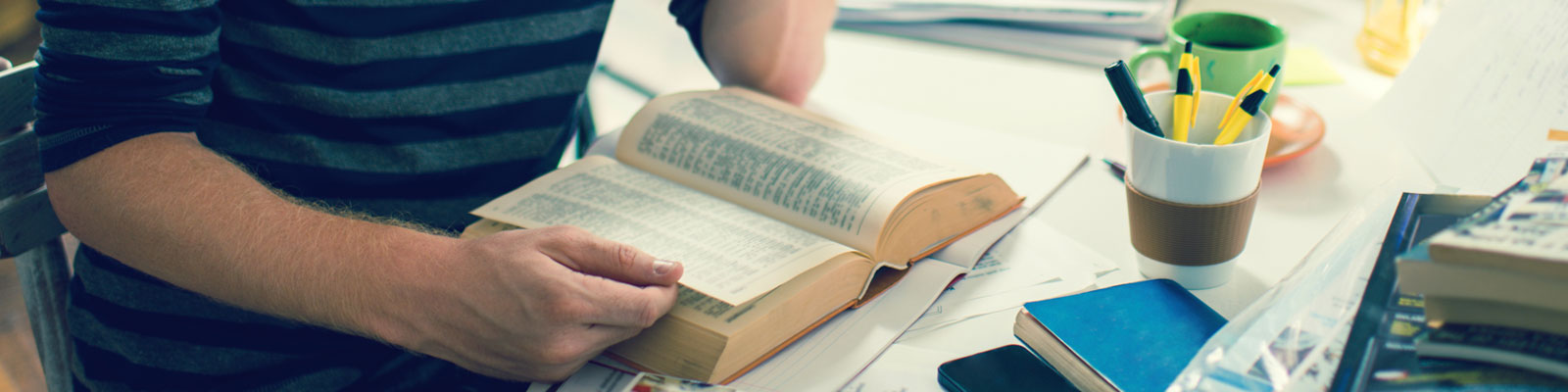 Jonge man zit aan tafel en leest boek