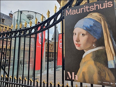 Hekwerk van het Mauritshuis met afbeelding van het Meisje met de Parel van Johannes Vermeer en daarachter een aantal banieren van de Open Universiteit